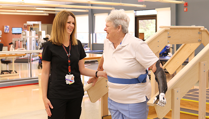 Patient Gayle Fisk works with a female therapist on climbing stairs with her prosthetic limbs.