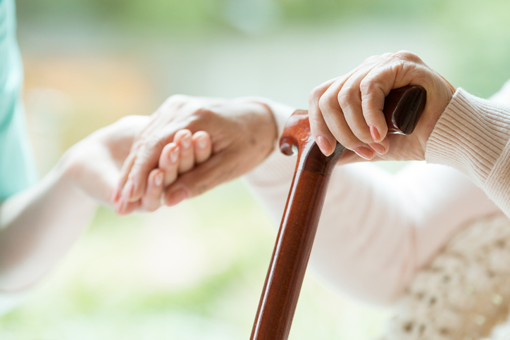Elder person supported on wooden stick during rehabilitation in friendly hospital