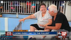 Screenshot of TV broadcast clip of caucasian female grinning and touching dolphin's nose