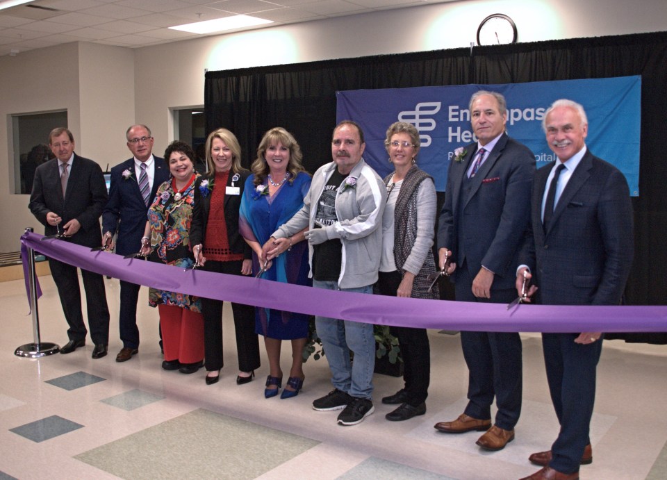 Nine people in business attire cutting purple ribbon and smiling