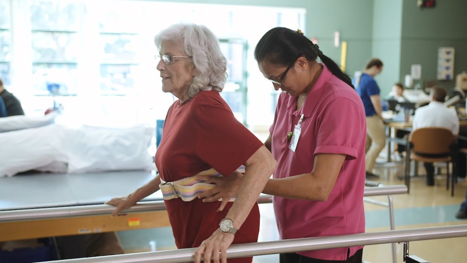 An Encompass Health therapist helps a patient to walk using parallel bars