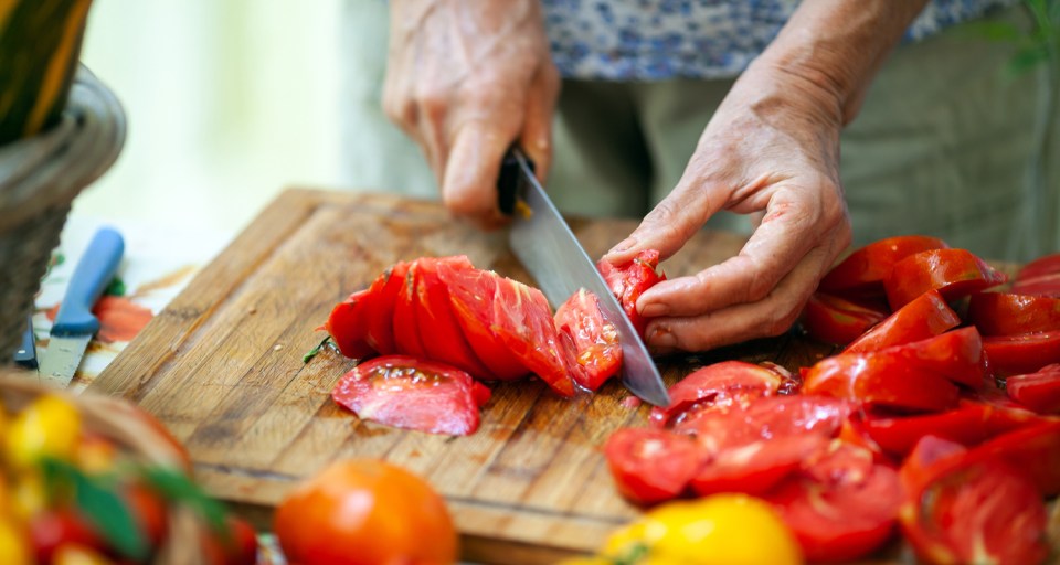Close-up of Senior Adult Woman Slicing Tomatoes on Cutting Board.