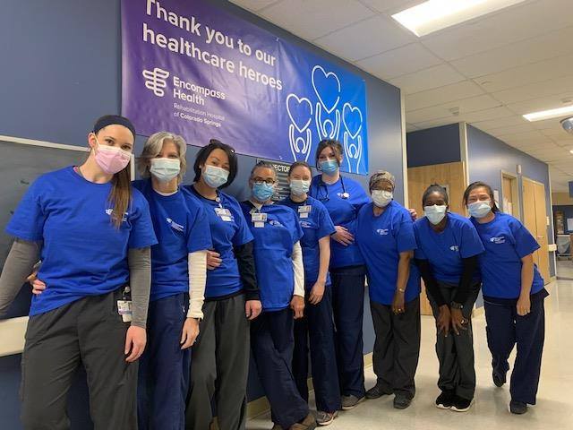 Group of employees in scrubs and masks pose under a healthcare heroes banner